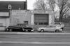 Two cars (an old one and a newer one) parked in front of an auto body shop.